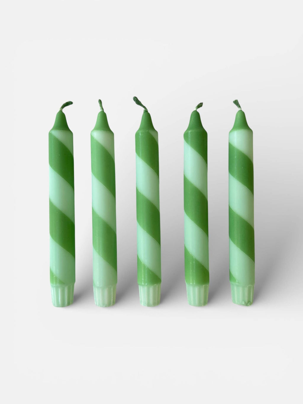 Five green and white striped candles on a light gray background
