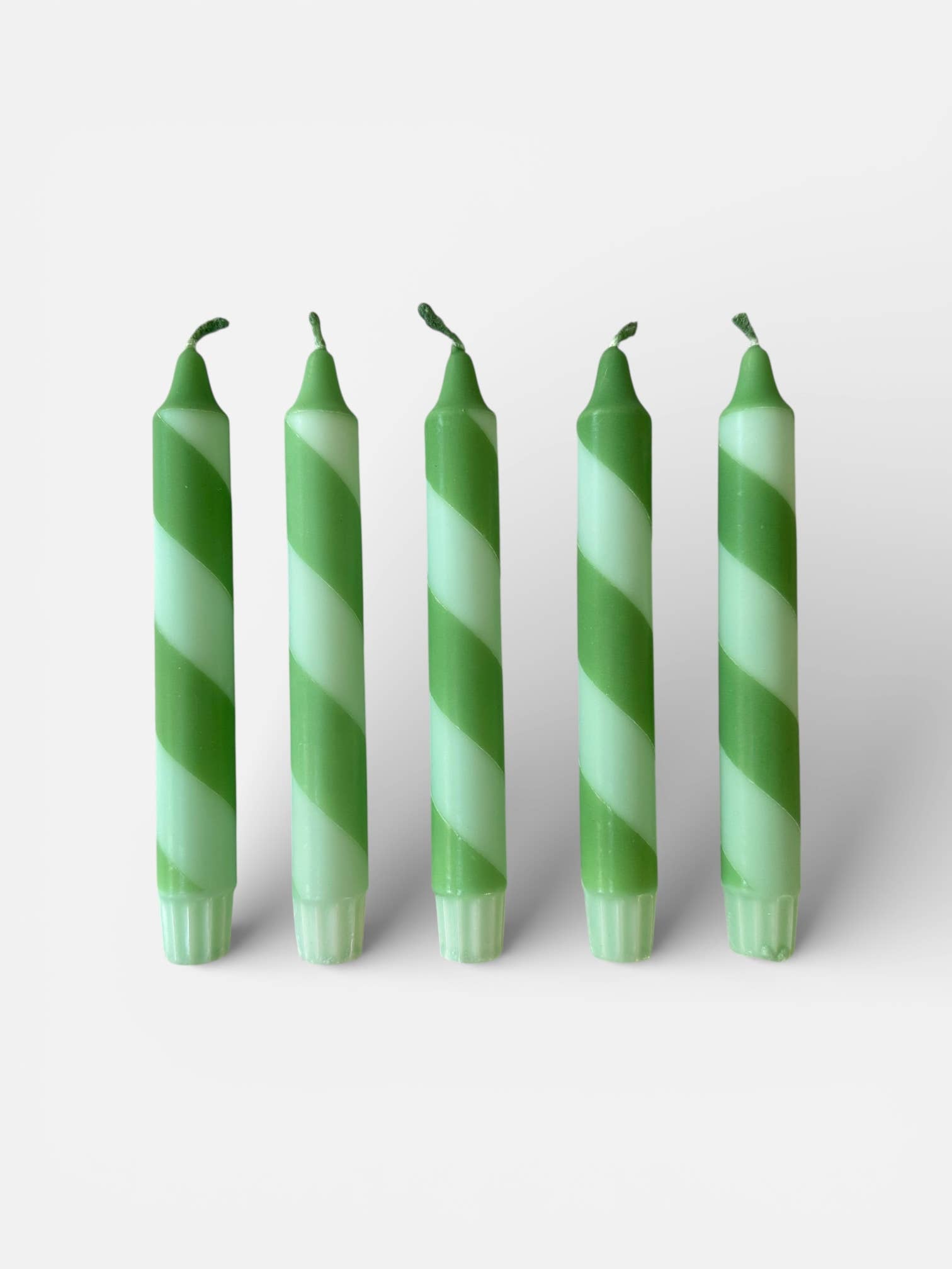 Five green and white striped candles on a light gray background