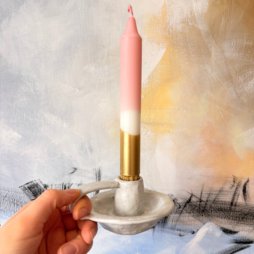 Hand holding a marble candle holder with a pink and gold candle against a textured background