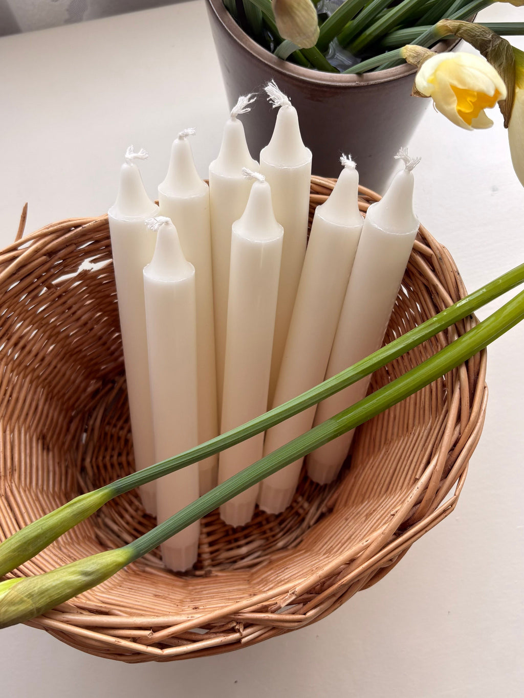 White candles in a wicker basket with flowers on a light surface